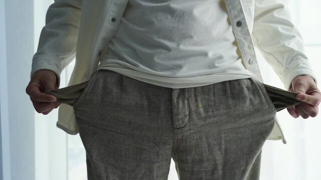 The man turns out his pants pockets and shows that there is no money there.
Empty pockets of a man.
Empty pockets in pants