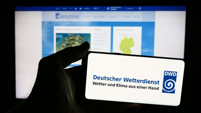 Stuttgart, Germany - 06-06-2024: Person holding mobile phone with logo of German meteorological service Deutscher Wetterdienst (DWD) in front of web page. Focus on phone display.