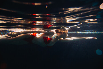 Young redheaded woman swimming underwater in a pool.