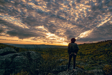 Human silhouette at sunset in a high place watching the sunset with a spring sky with broken clouds