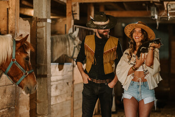 Young farmer couple with cat in hands walking at horse stable.