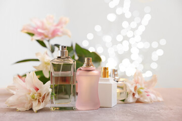 Perfume bottles and bouquet of beautiful lily flowers on table against beige background with blurred lights, closeup