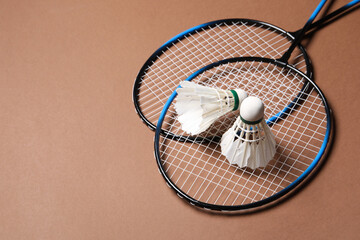 Feather badminton shuttlecocks and rackets on brown background, space for text