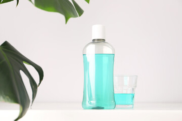 Bottle of mouthwash and glass on white table in bathroom