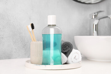 Bottle of mouthwash, toothbrushes and towels on white table in bathroom