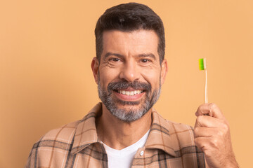 happy mature man showing ecological tooth brush in studio shot. biodegradable, hygiene concept. 