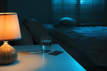 Insomnia treatment. Glass of water and pills on bedside table in bedroom at night © New Africa
