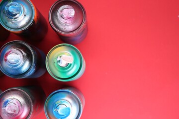 Many spray paint cans on red background, flat lay. Space for text