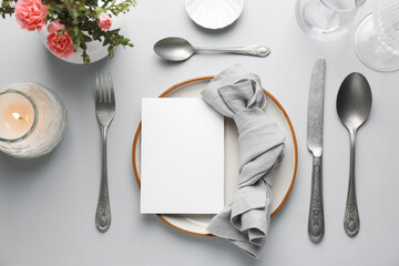 Empty menu, tableware, candle and floral decor on light grey table, flat lay. Mockup for design