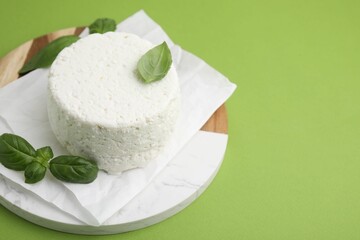 Fresh ricotta (cream cheese) and basil on green table, closeup. Space for text
