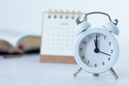 Alarm clock with calendar and holy bible book on white. Close-up. Christian biblical concept of time running, progress, patience, prayer, and Scripture study.