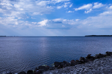 A tranquil sea view with a rocky shoreline under a partly cloudy sky, featuring distant sailboats on the calm water, ideal for showcasing the serenity of nature and coastal landscapes