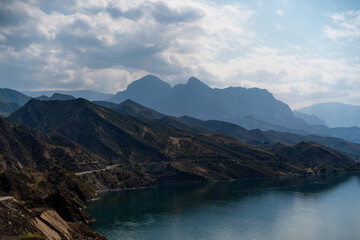 The mountains are covered in trees and the sky is cloudy. The water is calm and the mountains are in the background.