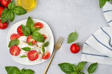 Salad of small balls of mozzarella, cherry tomatoes, basil and olive oil on a light background, top view, horizontal. Dish of Italian cuisine.