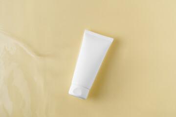 White mockup tube of cream in water on beige isolated background. The concept of natural cosmetics for the face, beauty products, advertising.