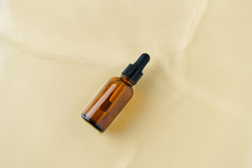 Brown glass jar with pipette dispenser of facial serum in water on beige isolated background. Skin nutrition and hydration concept, beauty and spa products