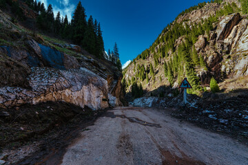 Dirt road in high mountains in spring, melting deep snow on edge of road