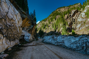 Dirt road in high mountains in spring, melting deep snow on edge of road
