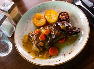 Fresh hot portion of ribs garnished with vegetables served on plate on table. Meat dish ready-to-eat.