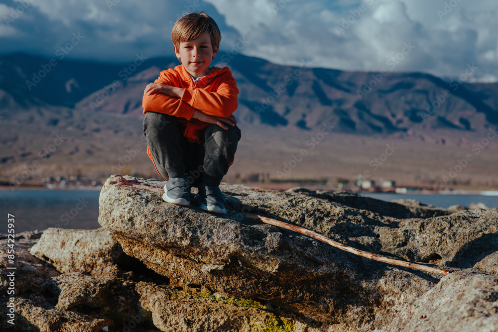 Canvas Prints Child tourist sitting on stone on lake shore and high mountains background at summer day