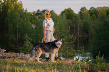 Young blonde girl with a Siberian Husky dog ​​on nature in summer day.