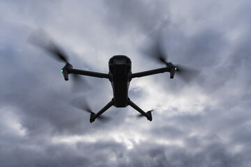 Silhouette of a drone with a camera in the air against a sky with clouds.