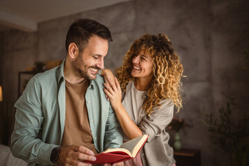 Boyfriend read a book while his girlfriend hug him at home