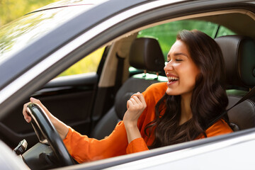 Attractive excited European woman riding her new car, having fun, enjoying listening music and...