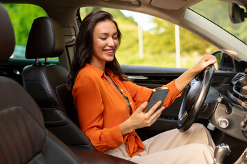 Happy woman driver using cellphone and browsing navigation app, sitting in automobile at drivers...