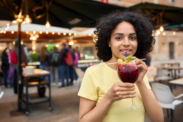 Young latin woman sipping a cocktail through a straw at an outdoor terrace