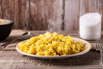 Plate with yellow rice with saffron, uncooked rice in a bowl, jar of salt and cutlery.