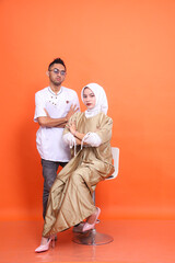 Elegant indonesia Muslim couple (man and woman) with arms crossed wearing kaftans and Muslim clothes in the month of Ramadan isolated on orange background. religious, fashion, advertising concepts