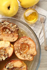Delicious baked quinces with nuts in bowl, honey and fresh fruits on wooden table, flat lay