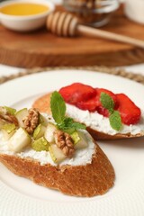 Delicious ricotta bruschettas with pear, strawberry and walnut on white table, closeup