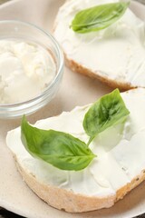 Delicious sandwiches with cream cheese and basil leaves on wooden table
