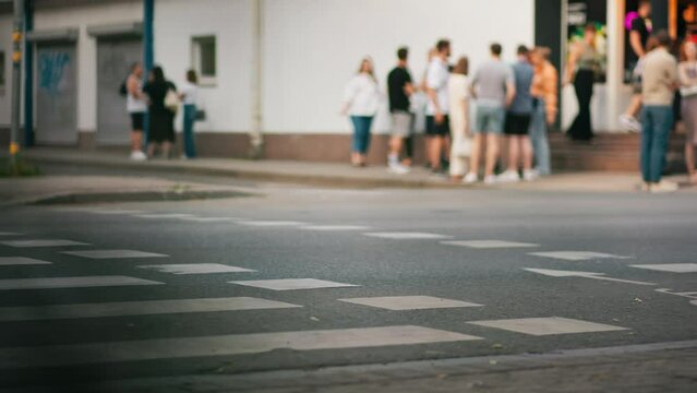 At a city junction, citizens gather, waiting to cross the street amidst everyday metropolitan motion