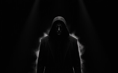 Creepy mysterious person wearing a hooded uniform standing in the middle of darkness.