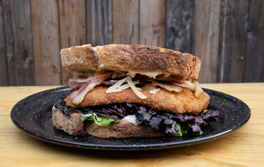 Delicious sandwich made with bread, parmesan cheese, lettuce, bacon and fried chicken steak, in a...