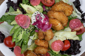 Sea salad background. Closeup view of a fresh salad with lettuce, cherry tomatoes, avocado, radish and onion pickles, seeds and cream cheese, in a white dish.