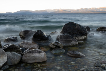 Long exposure shot of Nahuel Huapi lake at sunset. Beautiful blurred water effect, the rocky shore and dusk colors.