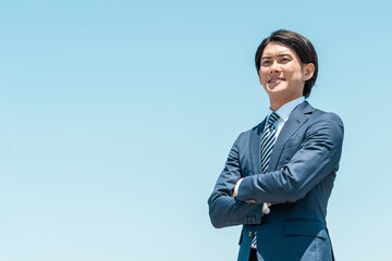 青空の中で腕組みする笑顔の若いアジア人ビジネスマン
