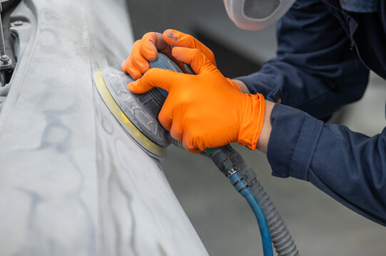 A mechanic sands the putty on a car body with a machine. Repair after an accident. 