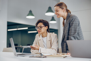 Fototapeta premium Two busy female coworkers discussing project while working in office and use laptop