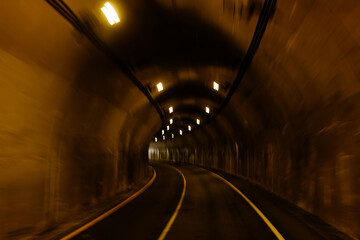 A long tunnel among the mountains. A light in the end of a tunnel. Industrial landscape. Asphalt road in the mountains. Highway. Driving through a tunnel among the mountains on a sunny summer day.