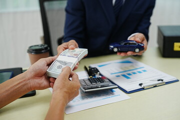 A businessman signs a contract for car insurance in an office. Holding a pen, he finalizes the agreement with the agent. This ensures protection and security for his new vehicle.