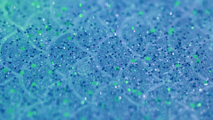Glitter fluid drip. Shiny gel texture. Blur blue color sparkling sequin grain particles in translucent liquid water emulsion spill abstract art background with bokeh lights.
