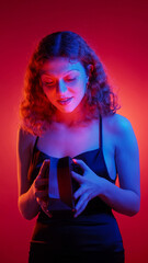 Valentine gift. Birthday present. Red blue neon color light surprised woman in evening dress opening jewelry bag isolated on gradient background.