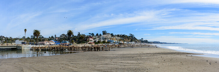 Scenic panoramic view of Rio Del Mar Beach near Santa Cruz California with a wooden pier stretching into water, flanked by coastal buildings and palms