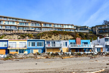 Beachfront houses overlook a sandy Rio Del Mar Beach strewn with debris. The front row of coastal home boarded up with plywood to prevent or reduce flood water damage