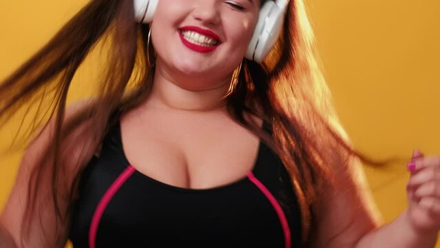 Music lover. Listening songs. Favorite playlist. Happy chubby overweight woman smiling enjoying melodies in headphones rhythmically dancing singing isolated on yellow background.